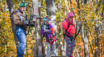 two girls and dad climbing ropes course in autumn